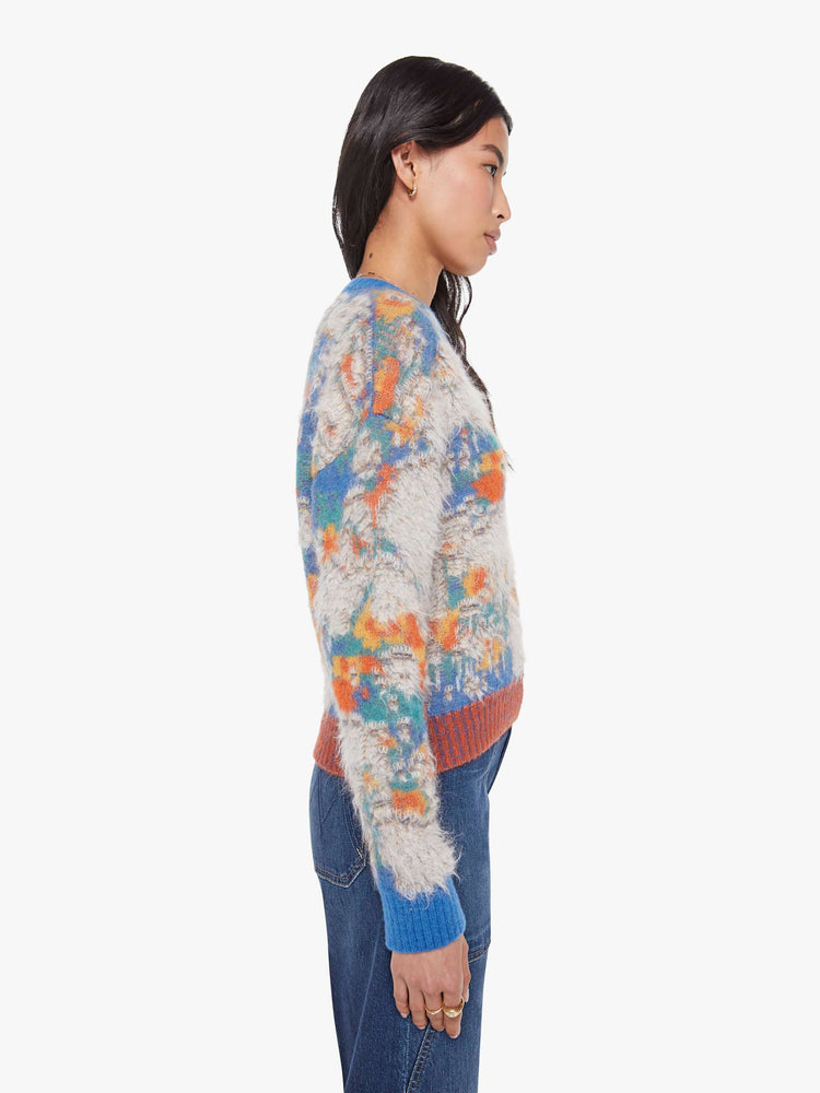Side view of a woman in a blue, yellow, orange and green graphic print sweater  with fuzzy, distressed details inspired by a well-worn rug. 