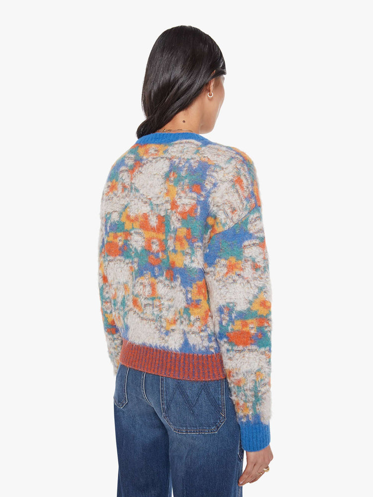 Back view of a woman in a blue, yellow, orange and green graphic print sweater  with fuzzy, distressed details inspired by a well-worn rug. 