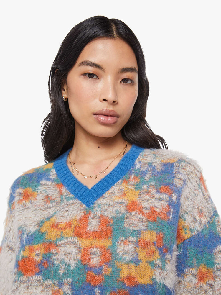 Close up view of a woman in a blue, yellow, orange and green graphic print sweater  with fuzzy, distressed details inspired by a well-worn rug. 