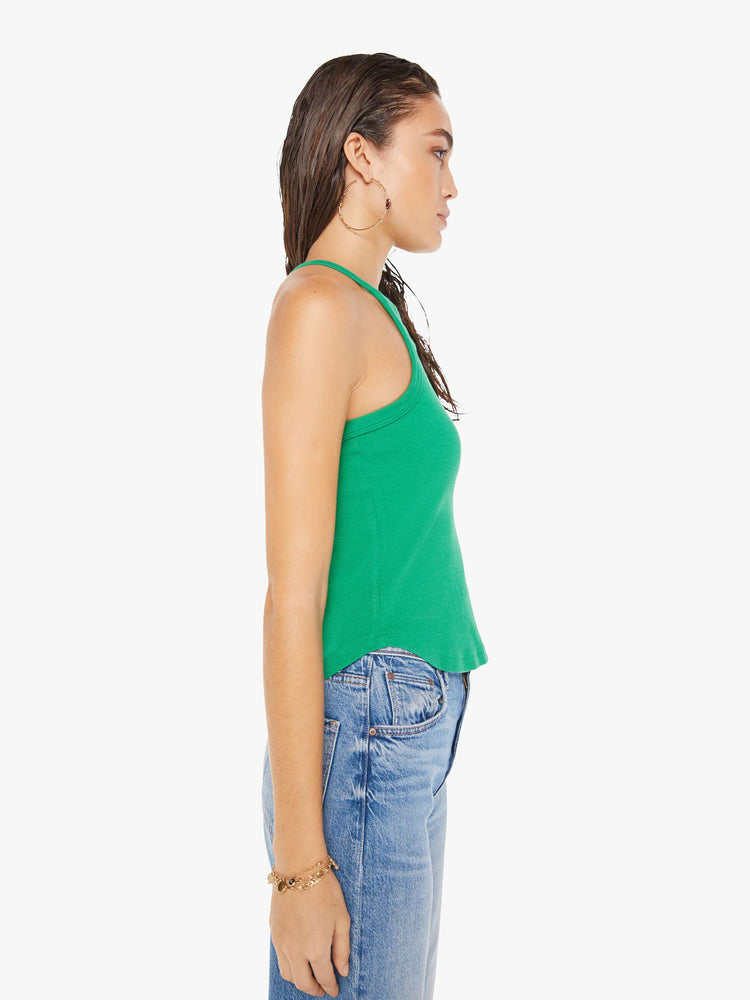 Side view of a woman wearing a green ribbed tank top with a cropped curved hem, paired with a medium blue wash jean.