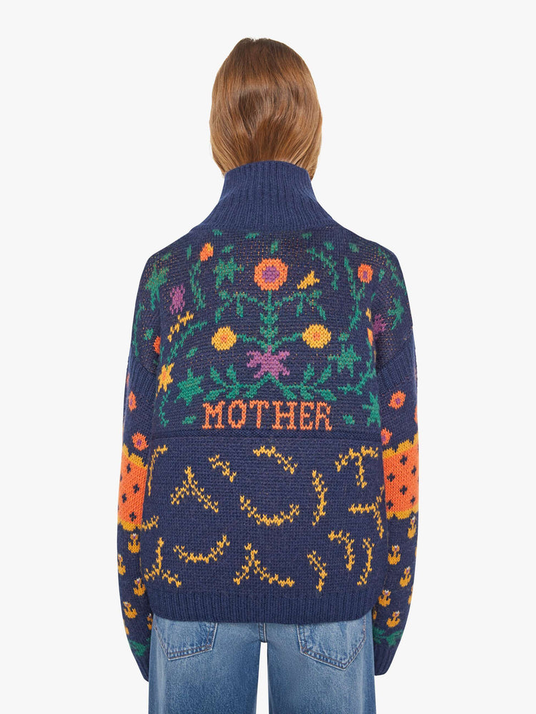 Back view of a woman in a navy blue turtleneck sweater with a high neck, drop shoulders, extra-long sleeves, ribbed hems and an oversized fit.