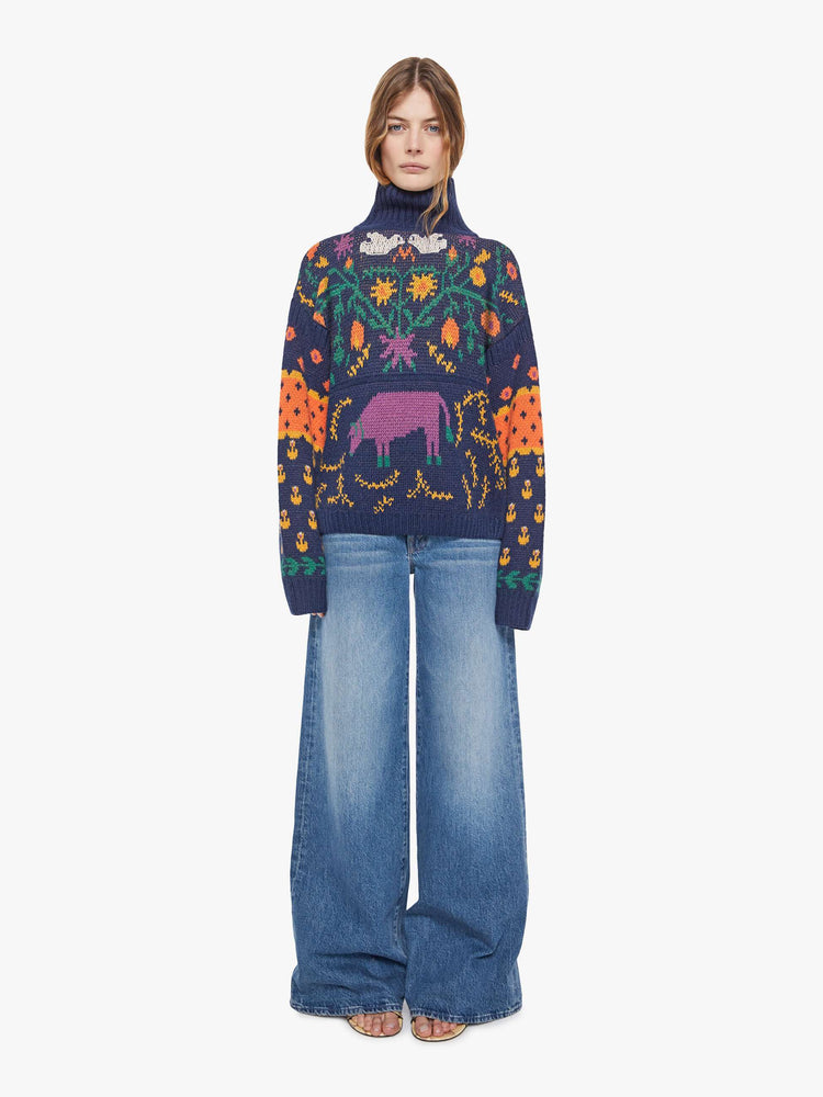 Full body view of a woman in a navy blue turtleneck sweater with a high neck, drop shoulders, extra-long sleeves, ribbed hems and an oversized fit.