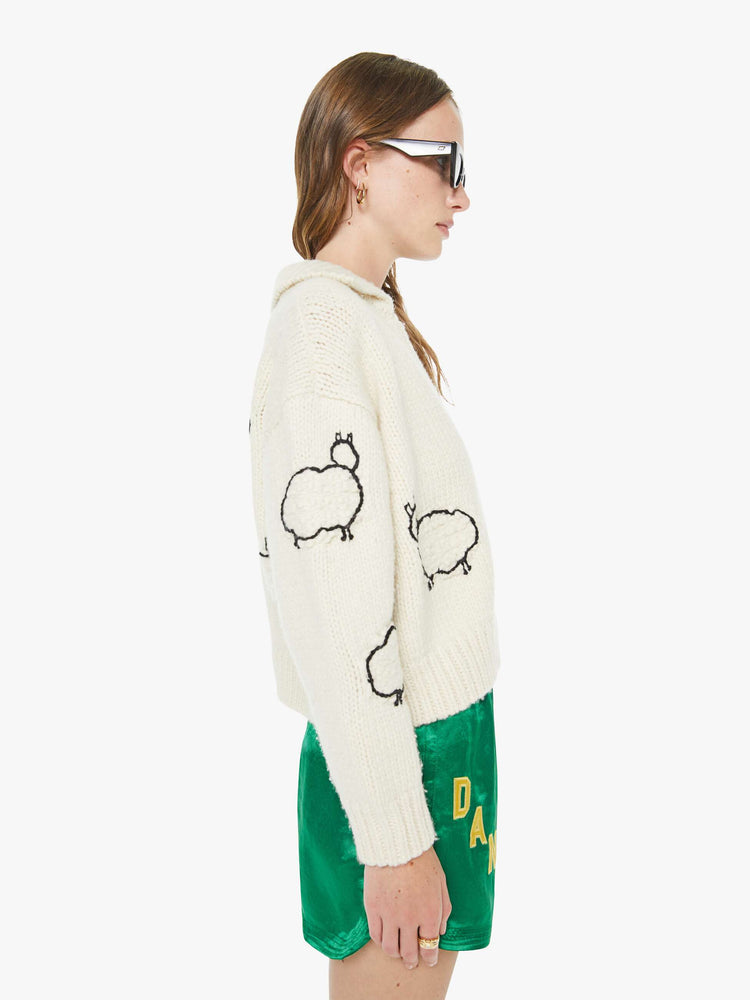 Side view of a woman in an off white  with black sheep silhouettes throughout collared cardigan with ribbed hems, buttons down the front and a cropped fit.