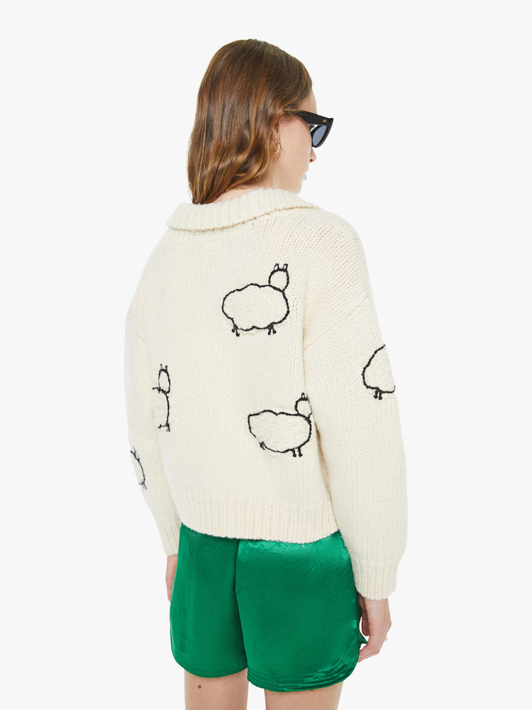 Back view of a woman in an off white  with black sheep silhouettes throughout collared cardigan with ribbed hems, buttons down the front and a cropped fit.