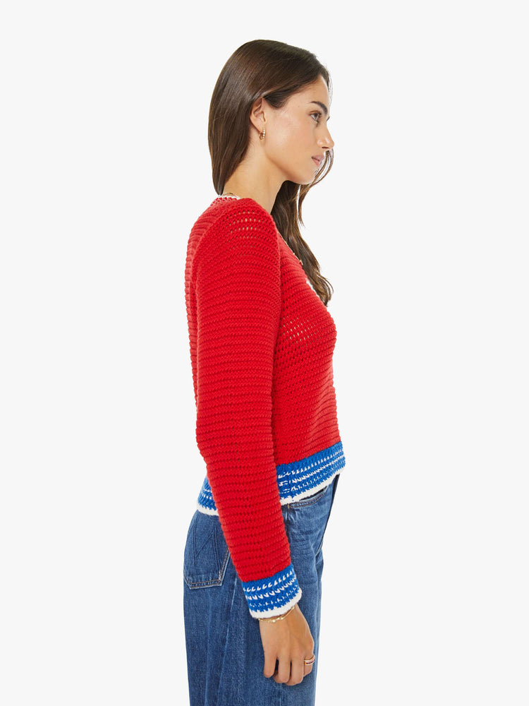 Side view of a woman in a bright red with blue and white trim and a martini glass in white on the front sweater with long sleeves and a cropped fit. 