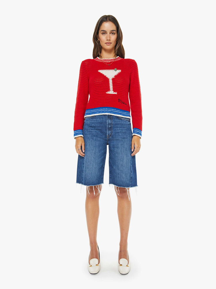 Full body view of a woman in a bright red with blue and white trim and a martini glass in white on the front sweater with long sleeves and a cropped fit. 