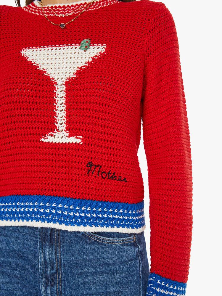 Close up view of a woman in a bright red with blue and white trim and a martini glass in white on the front sweater with long sleeves and a cropped fit. 