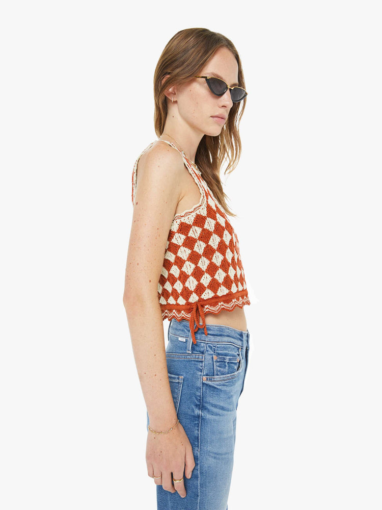 Side view of a woman in a burnt orange and off white sleeveless, square-neck top with thick straps, tie details on the sides and a super cropped fit.