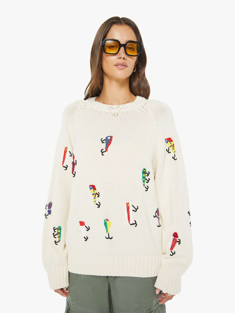 Front view of a woman in an off-white sweater designed with colorful fishing lure embroidery throughout.