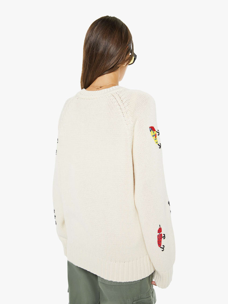 Back view of a woman in an off-white sweater designed with colorful fishing lure embroidery throughout.