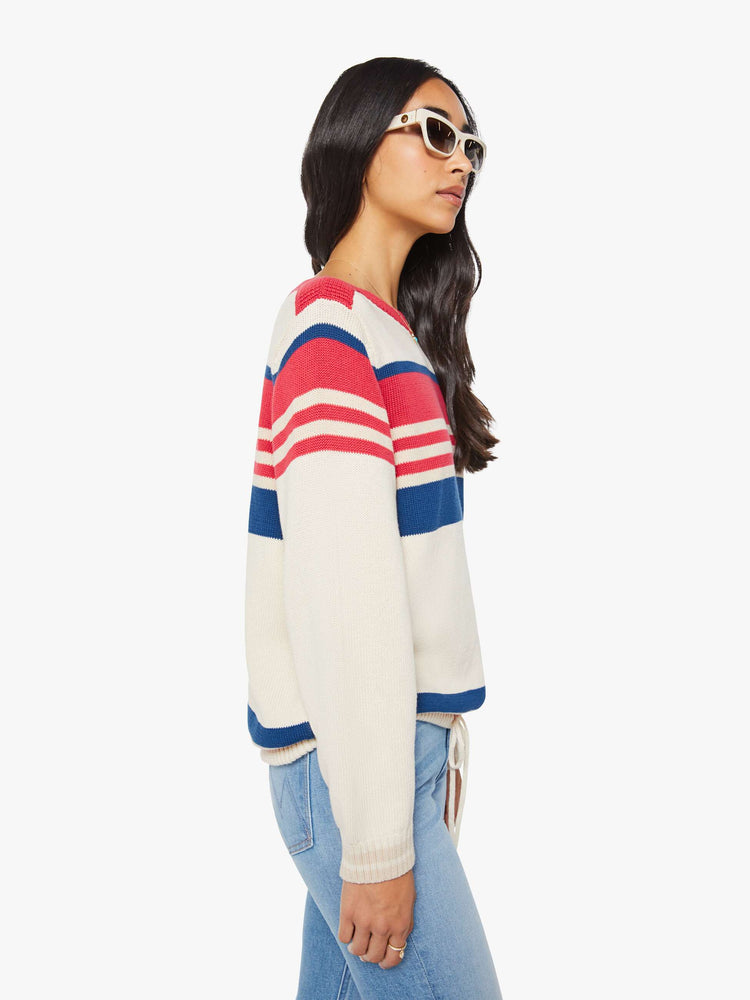 Side view of a woman in off-white with red and blue horizontal stripes long-sleeve sweater with a boat neck, drop shoulders, ribbed hems, a drawstring waist and an oversized fit.