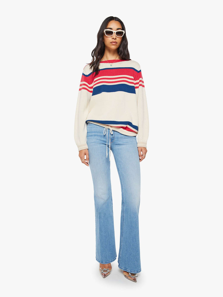 Full body view of a woman in off-white with red and blue horizontal stripes long-sleeve sweater with a boat neck, drop shoulders, ribbed hems, a drawstring waist and an oversized fit.