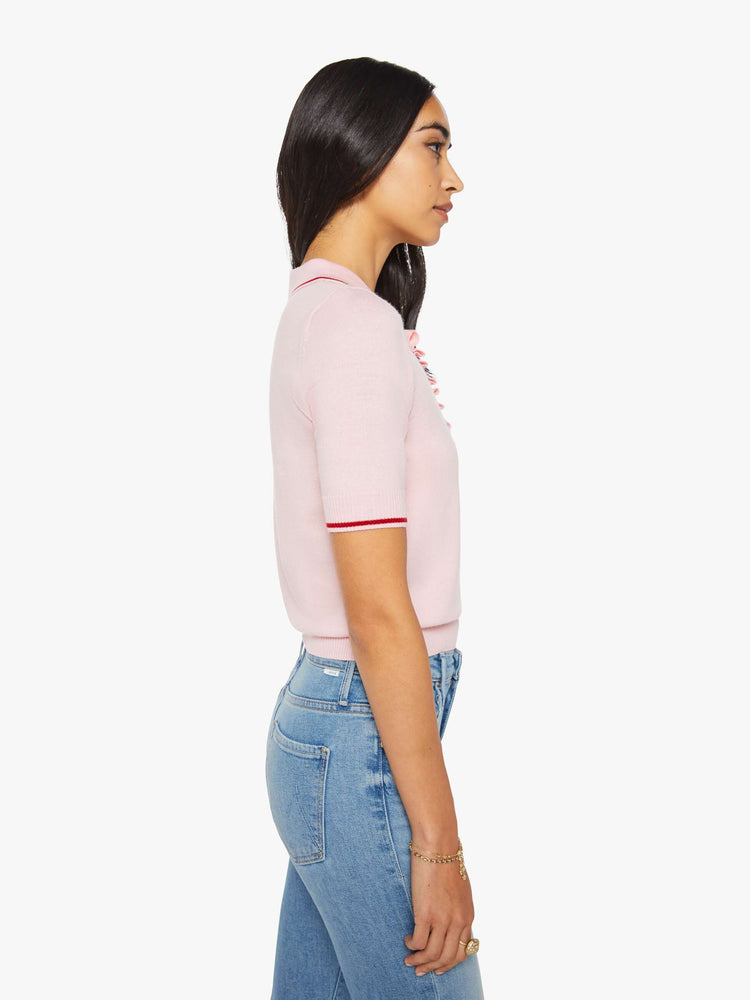 Side view of a woman in a light pink and red short sleeve polo with a buttoned V-neck, ruffle details, ribbed hems and a slightly cropped fit.