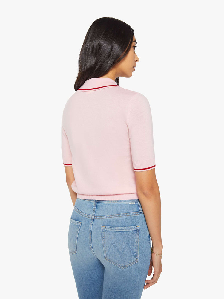 Back view of a woman in a light pink and red short sleeve polo with a buttoned V-neck, ruffle details, ribbed hems and a slightly cropped fit.