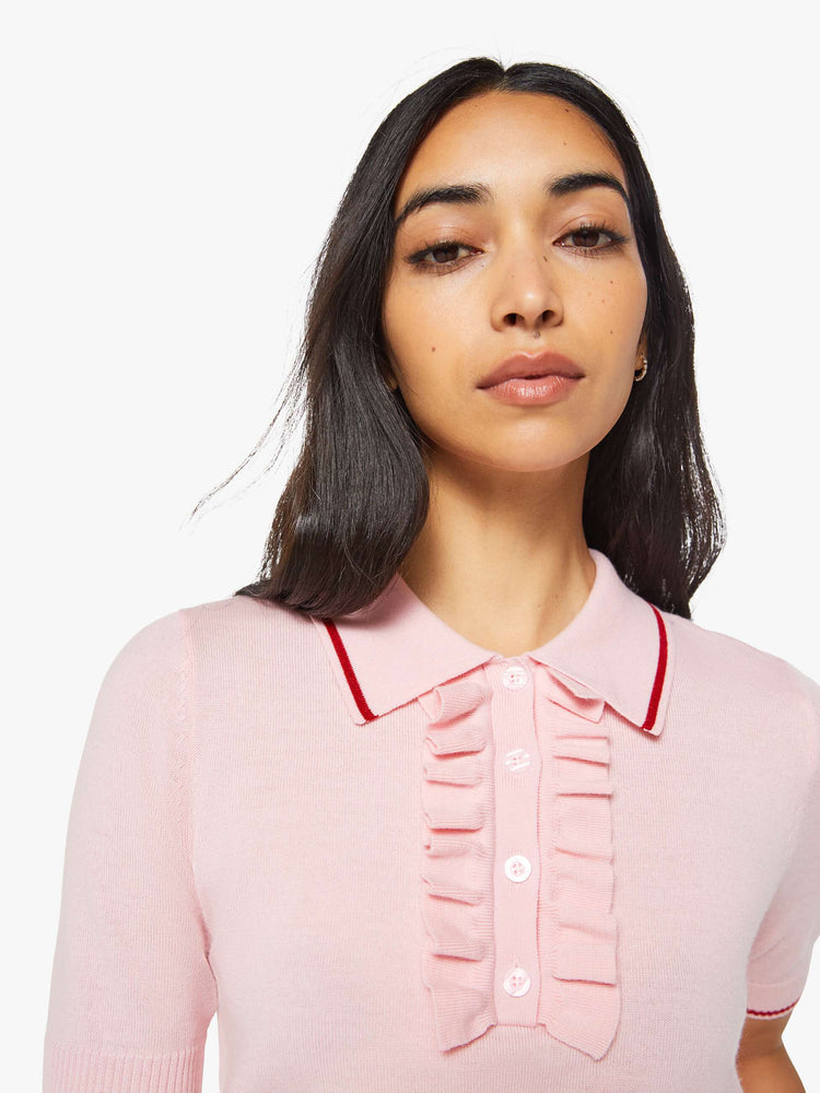 Close up view of a woman in a light pink and red short sleeve polo with a buttoned V-neck, ruffle details, ribbed hems and a slightly cropped fit.