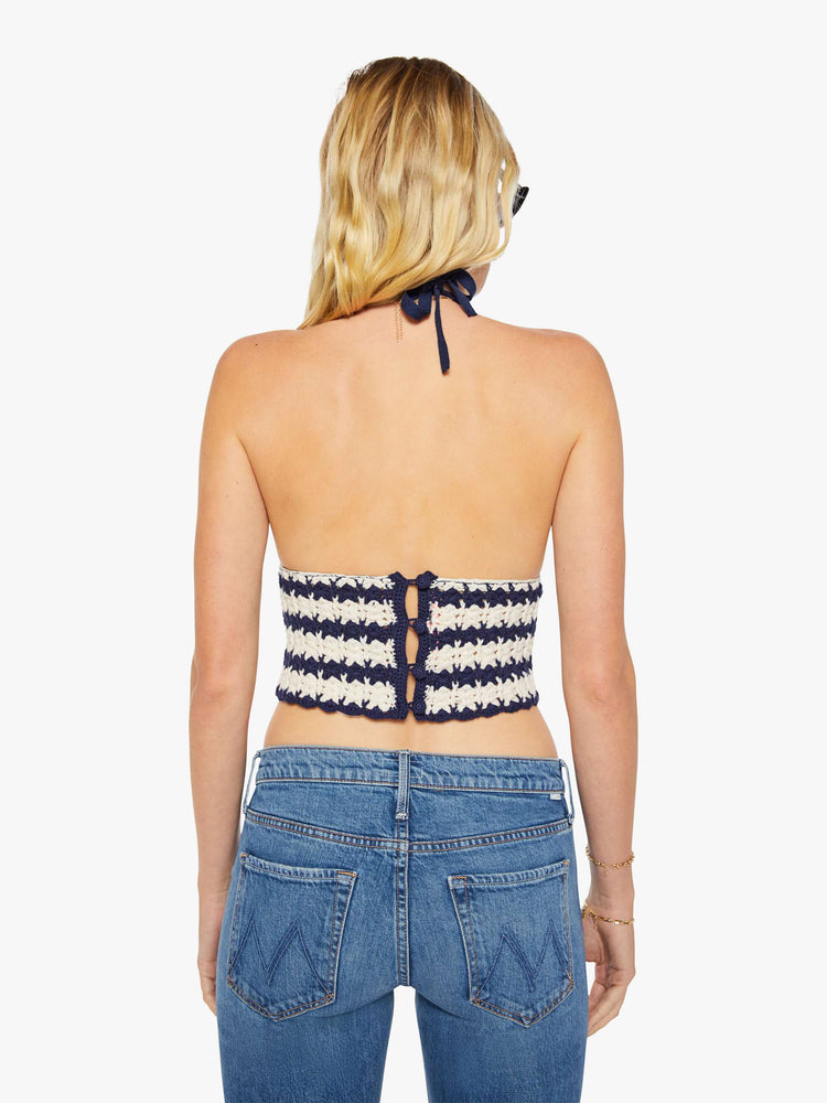 Back view of a woman in a navy and off white stripes knit halter top with thin straps and a cropped, narrow fit.