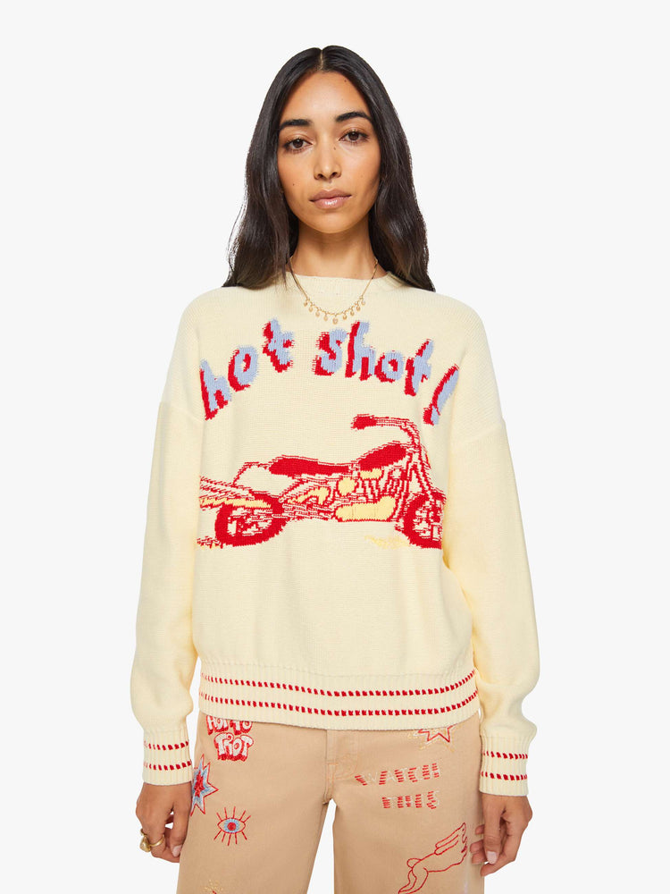 Front view of a woman in a butter yellow with red and baby blue text, a motorcycle graphic and decorative trim sweater.