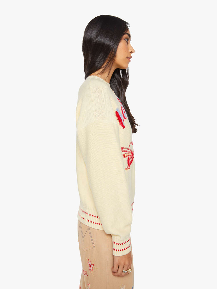 Side view of a woman in a butter yellow with red and baby blue text, a motorcycle graphic and decorative trim sweater.