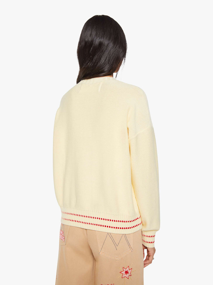 Back view of a woman in a butter yellow with red and baby blue text, a motorcycle graphic and decorative trim sweater.