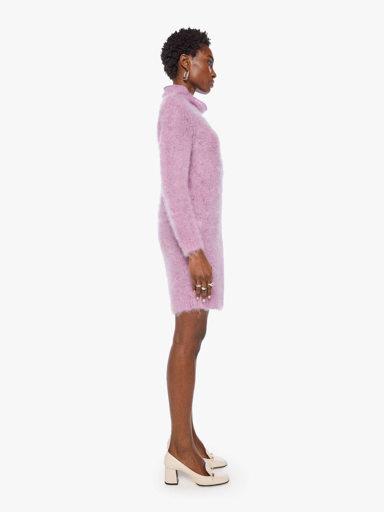 Side view of a woman in a light lavender mini dress with a soft turtleneck, long sleeves, an open back and a thigh-grazing hem.