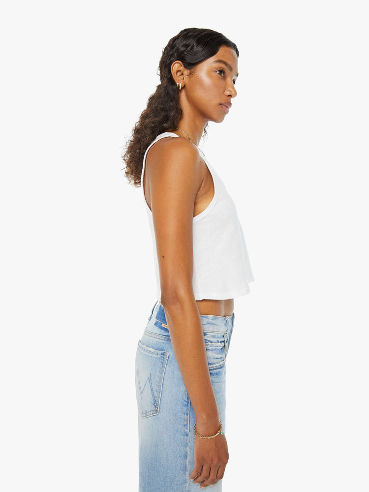 Side view of a woman in a white scoop-neck tank top with a cropped hem and a loose fit.