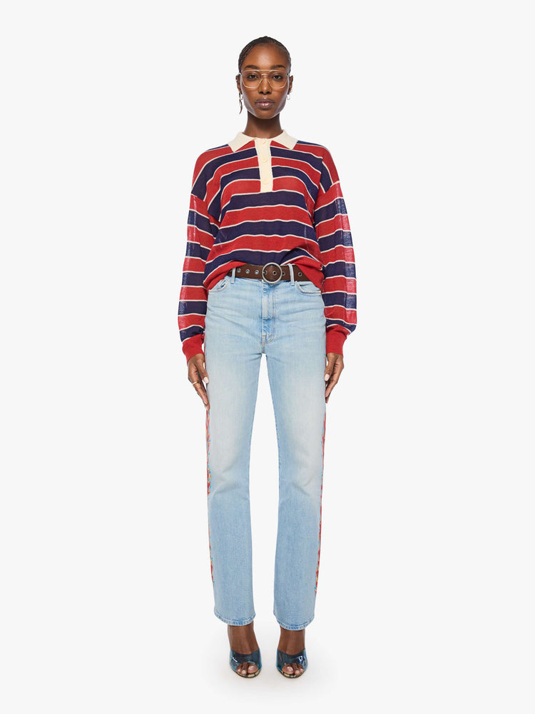 Full body view of a woman in a red and navy stripes with a cream collar and button placket rugby polo with this long-sleeve top featuring drop shoulders and an oversized fit.