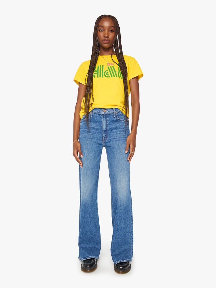 Full body view of a woman bright yellow tee features a pink and green text graphic on the front.