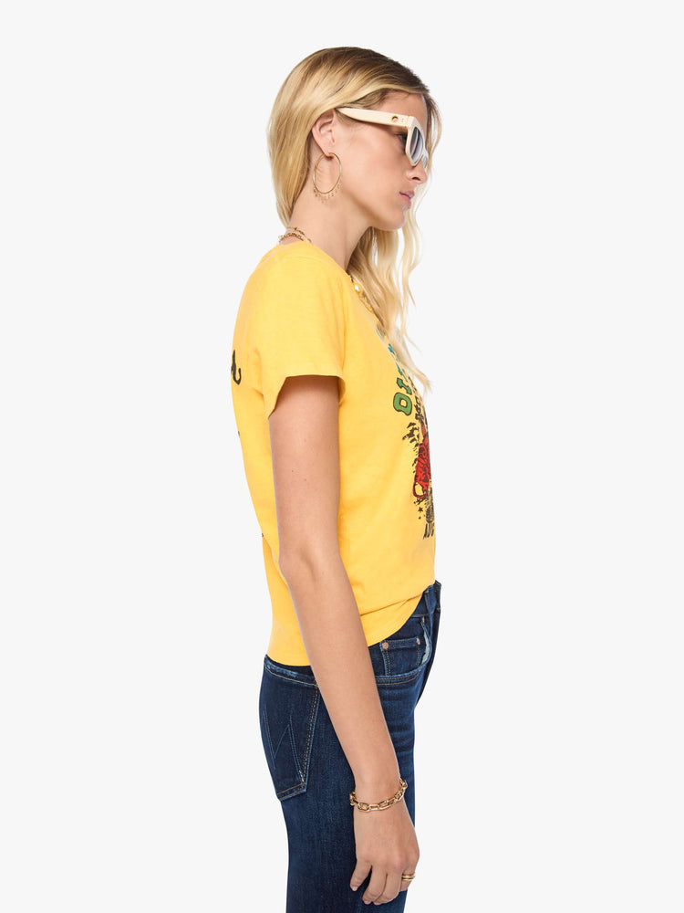 Side view of a woman in a golden yellow tee features a colorful graphic inspired by motorcycle rally race merch.