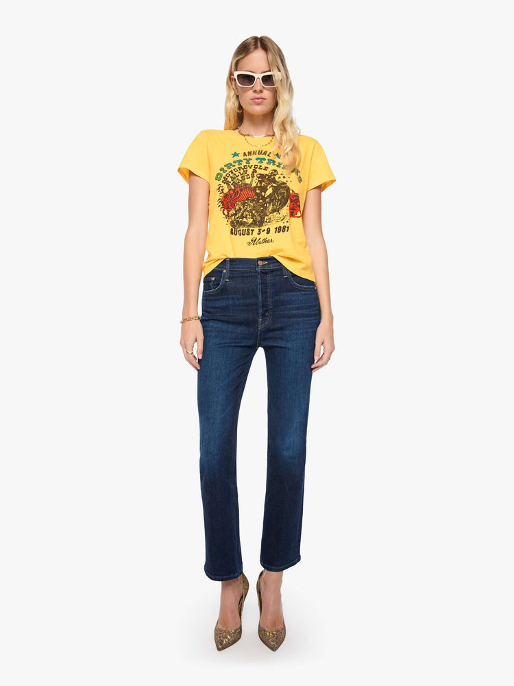 Full body view of a woman in a golden yellow tee features a colorful graphic inspired by motorcycle rally race merch.