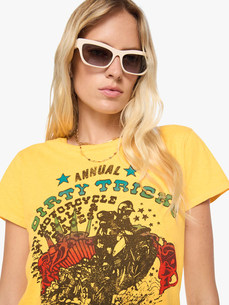 Close up view of a woman in a golden yellow tee features a colorful graphic inspired by motorcycle rally race merch.