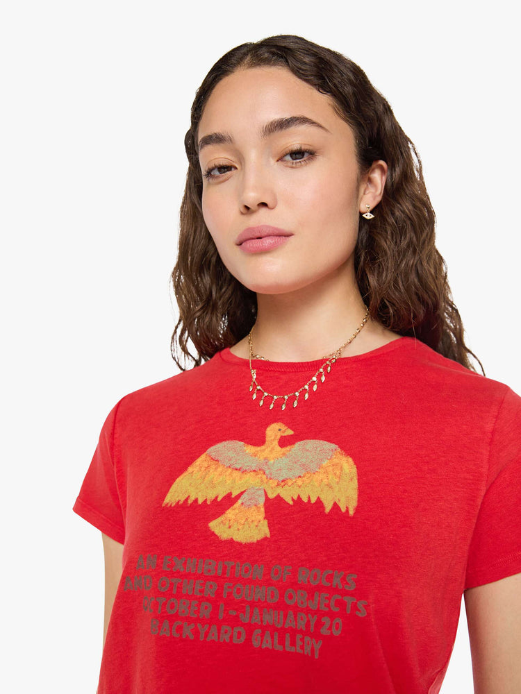 Close up view of a woman in red tee features a bird graphic and text in grey on the front.