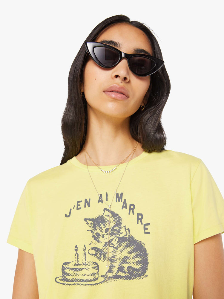 Close up view of a woman in a pale yellow tee features a kitten graphic and text in French on the front.