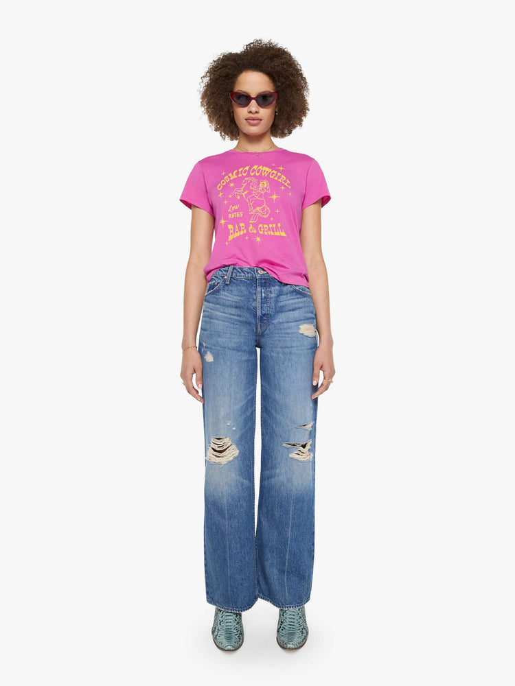 Full body view of a woman in a bright pink tee with a celestial saloon graphic in yellow across the chest.