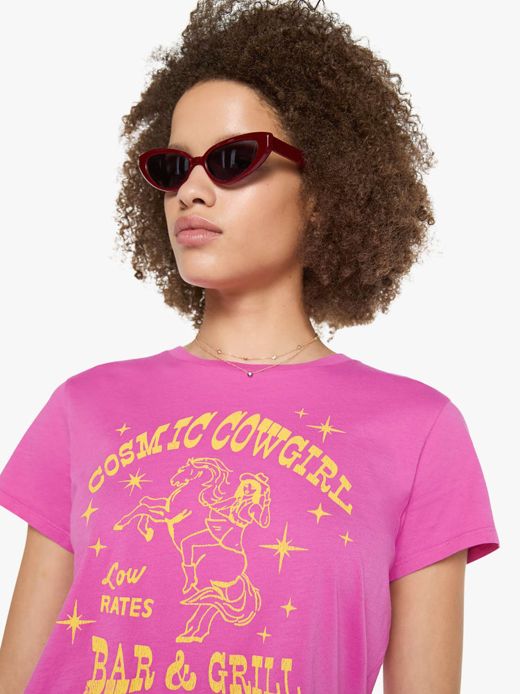 Close up view of a woman in a bright pink tee with a celestial saloon graphic in yellow across the chest.