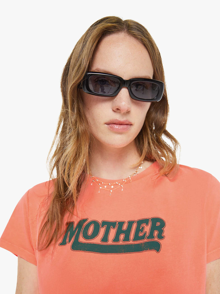 Close up view of a woman in a neon orange tee features MOTHER's name in green on the front. 