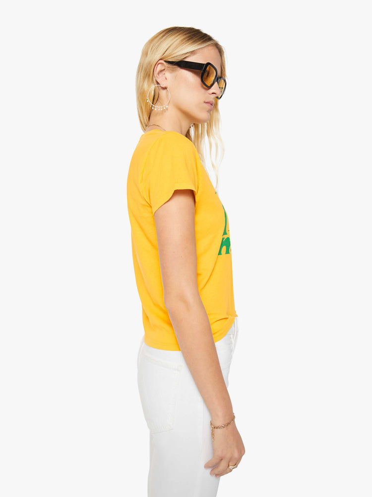 Side view of a woman in a golden yellow tee features a green text graphic on the front.
