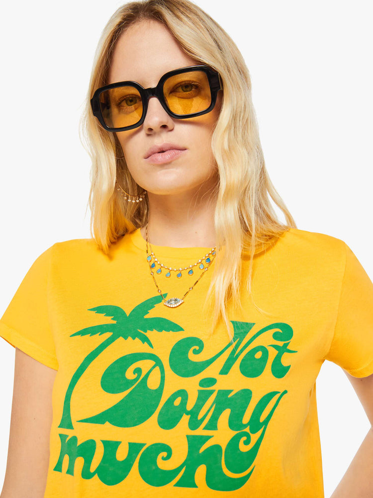 Close up view of a woman in a golden yellow tee features a green text graphic on the front.