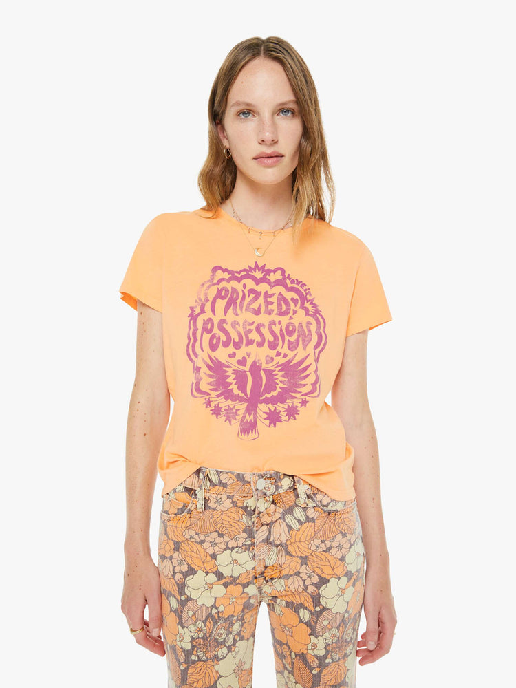 Front view of a woman in a  faded orange tee features a purple bird graphic with text on the front.