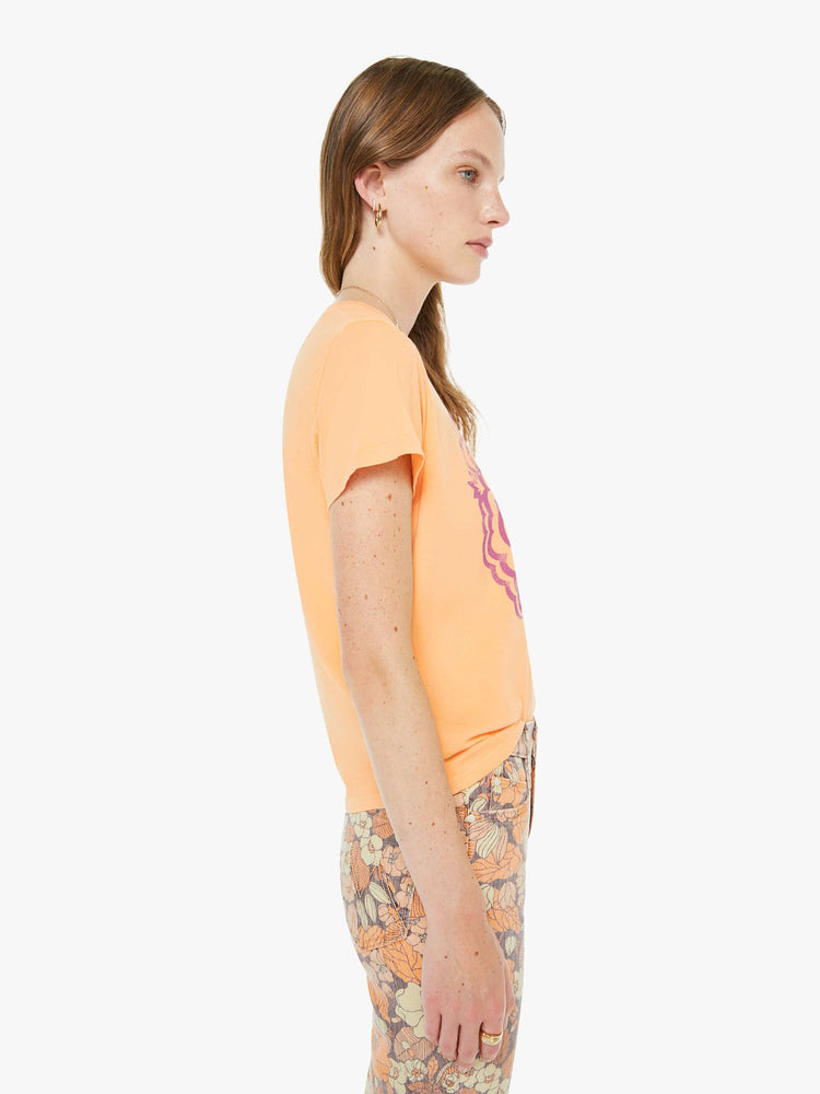 Side view of a woman in a  faded orange tee features a purple bird graphic with text on the front.