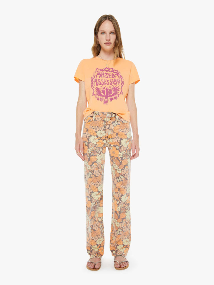 Full body view of a woman in a  faded orange tee features a purple bird graphic with text on the front.