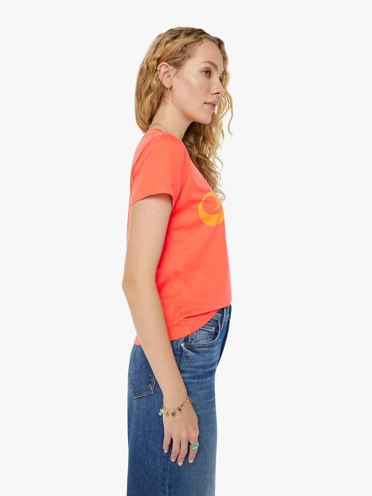 Side view of a woman in a slightly sheer orange crewneck with a slim fit featuring a text graphic "Spritz" in yellow styled with blue jeans.