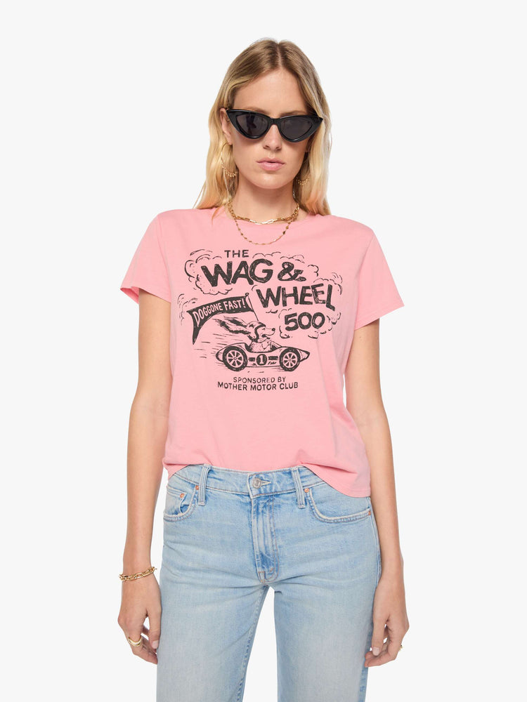 Front view of woman in baby pink tee features a faded black graphic of a dog in a racecar with text on the front.