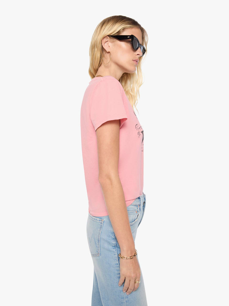 Side view of woman in baby pink tee features a faded black graphic of a dog in a racecar with text on the front.