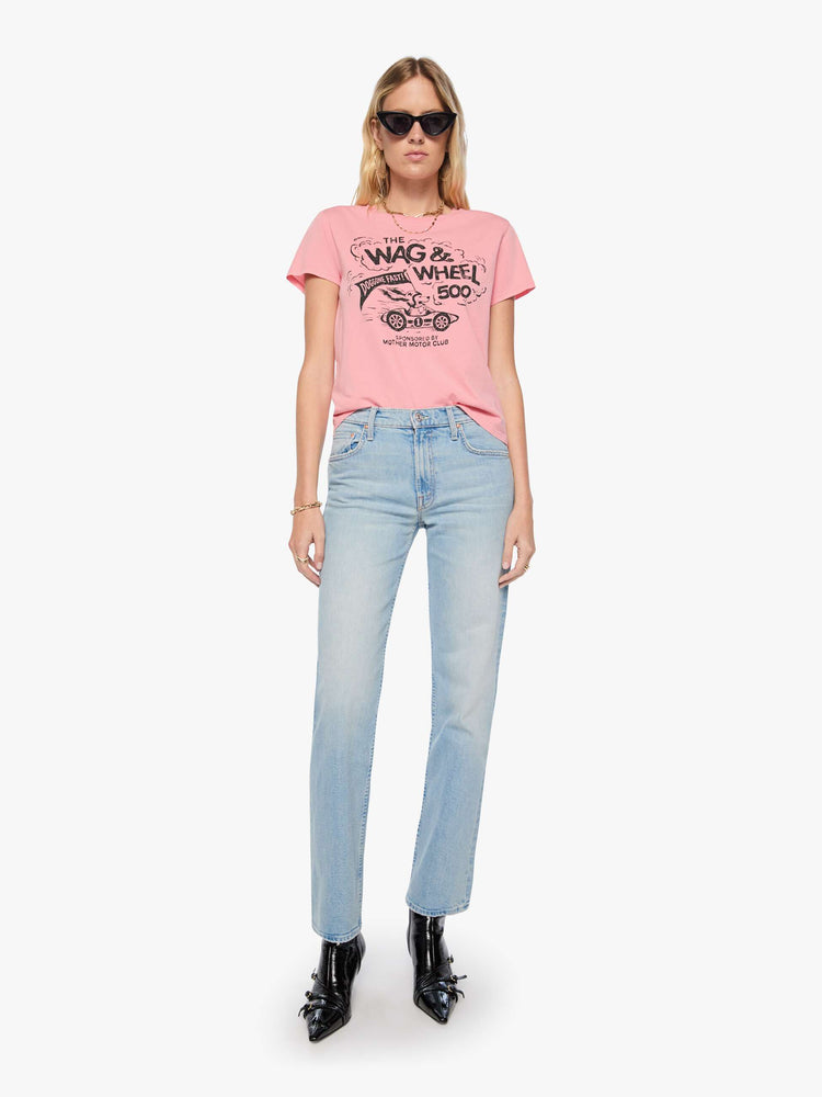 Full body view of woman in baby pink tee features a faded black graphic of a dog in a racecar with text on the front.