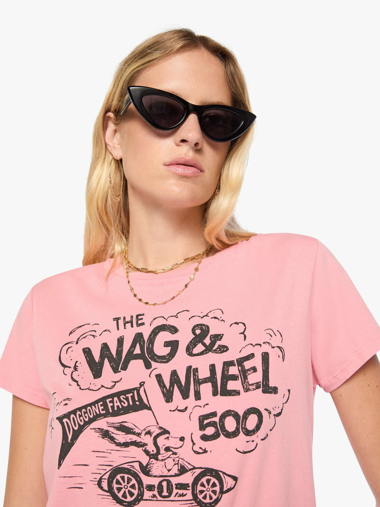 Close up view of woman in baby pink tee features a faded black graphic of a dog in a racecar with text on the front.