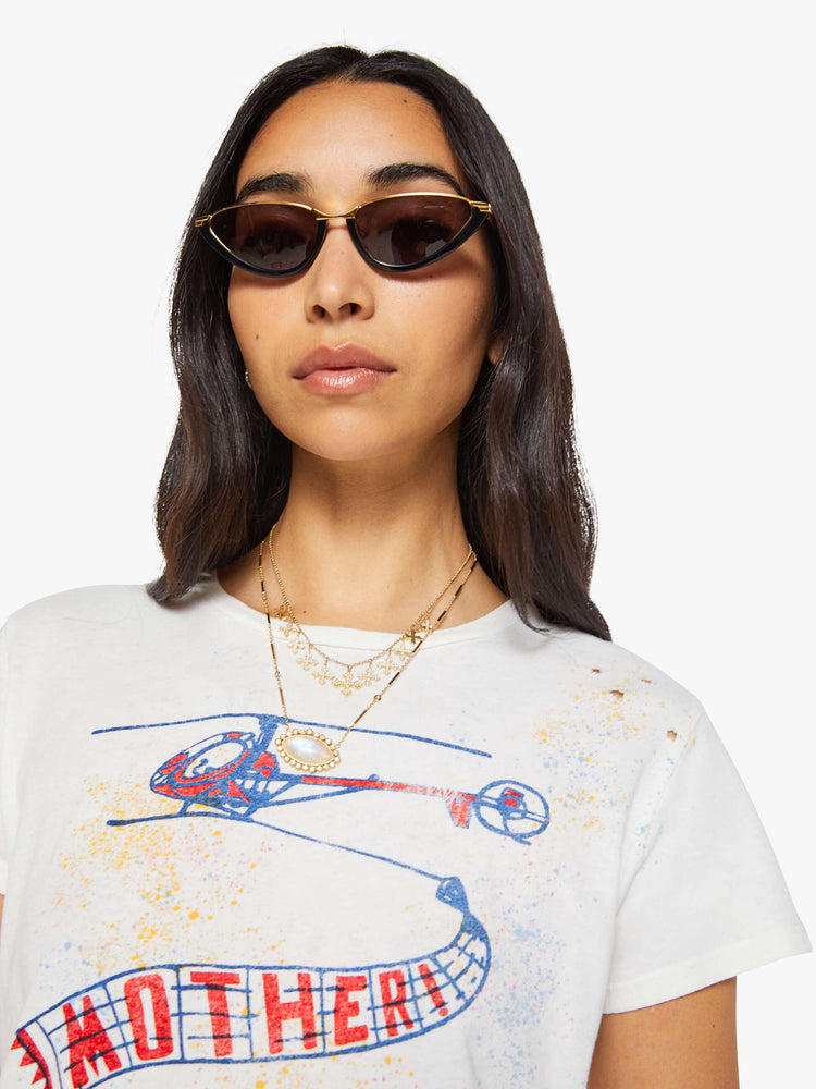 Close up view of a woman in off-white tee features a blue and red vintage-inspired helicopter graphic and MOTHER's name on the front, colorful paint splatters and distressed details throughout.