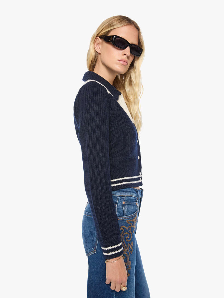 Side view of a woman in a navy with an angled white yoke and stripes at the hems, cropped cardigan with snap closures.