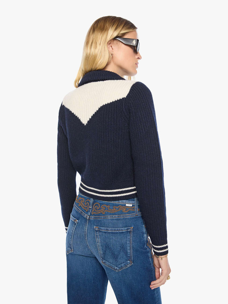 Back view of a woman in a navy with an angled white yoke and stripes at the hems, cropped cardigan with snap closures.