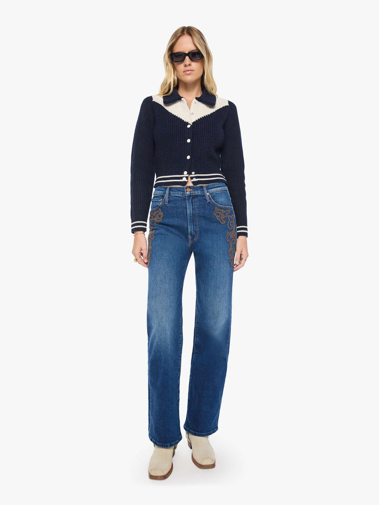 Full body view of a woman in a navy with an angled white yoke and stripes at the hems, cropped cardigan with snap closures.