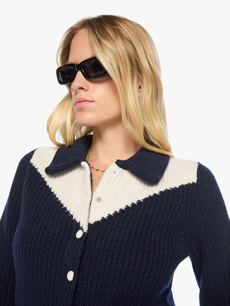 Close up view of a woman in a navy with an angled white yoke and stripes at the hems, cropped cardigan with snap closures.